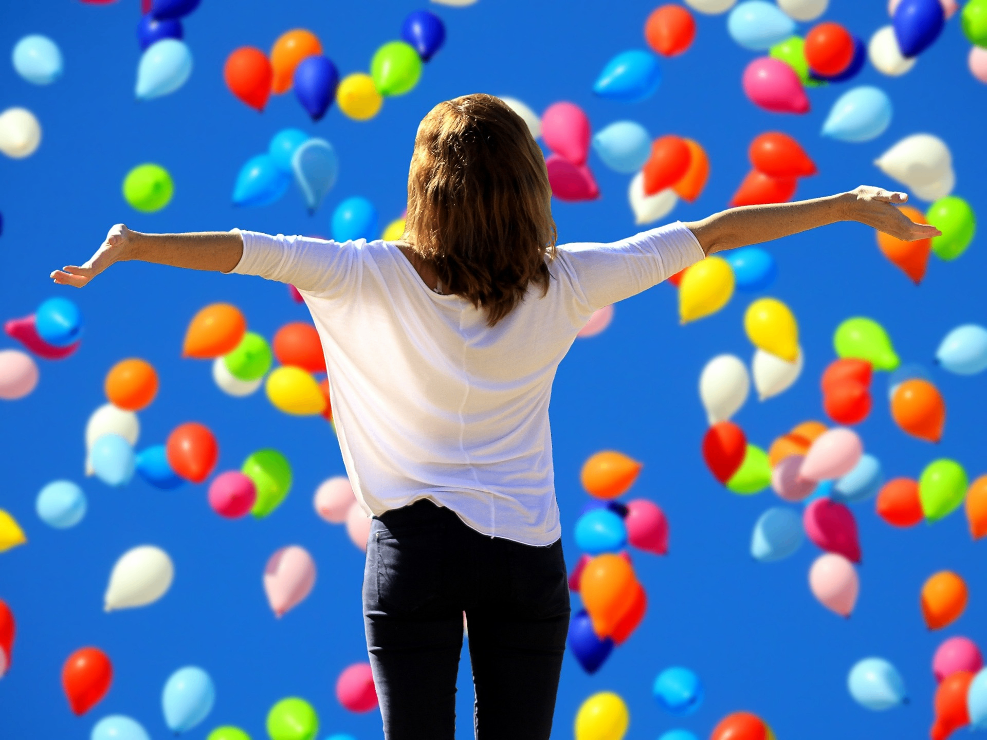 Femme bras ouverts entourée de ballons colorés, évoquant la joie et la liberté retrouvées